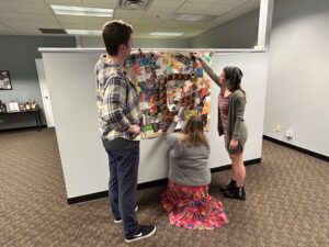 Steve, Mariah, and Alyssa come together to apply recycled silver foil and more labels to the mural.