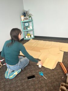 Intern - Victoria Leu is helping piece together the recycled kraft label material for the sustainable mural.